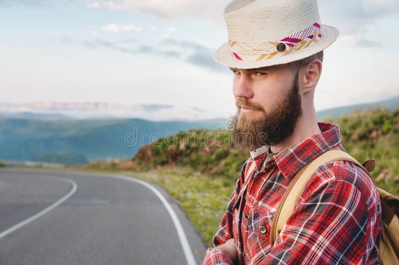 Portret van een bebaarde, gelukkige, serieuze reiziger hipster met een rugzak in een pleister shirt en een hoed naast een onbeken
