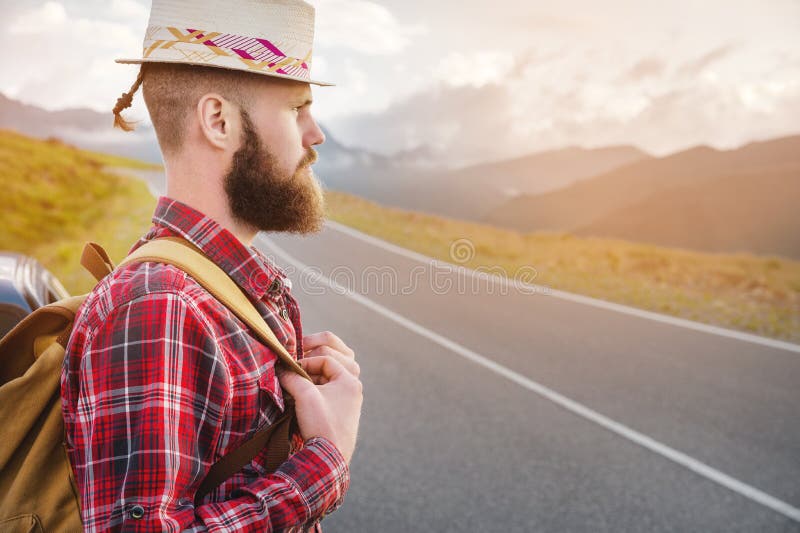 Portret van een bebaarde, gelukkige, serieuze reiziger hipster met een rugzak in een pleister shirt en een hoed naast een onbeken