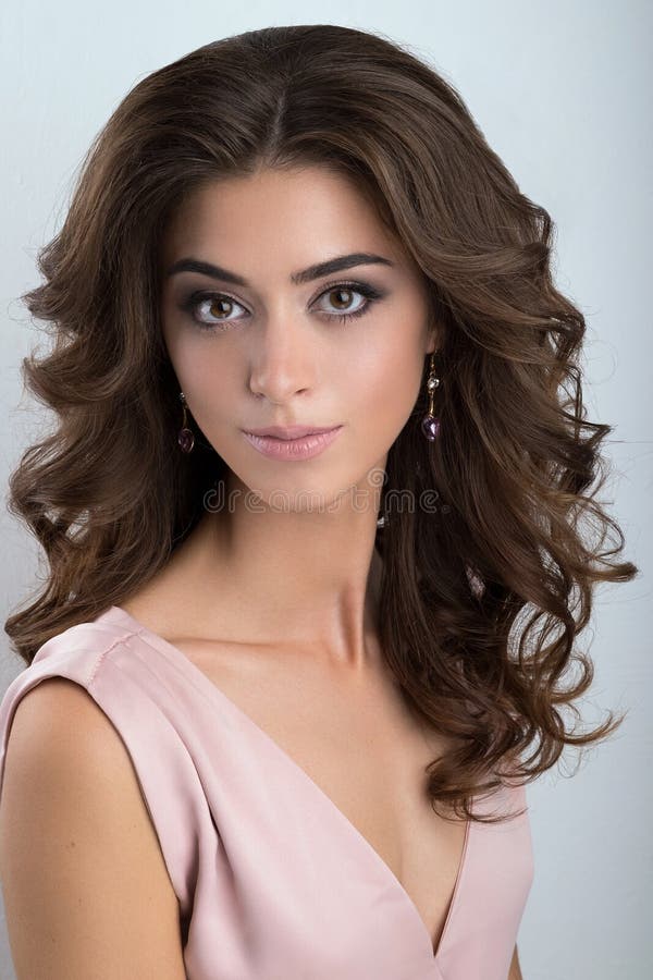 Portret van een brunette met omvangrijke krullen en een zachte samenstelling in een lichtrose kleding stock afbeelding Portret van een brunette met omvangrijke krullen en een zachte samenstelling in een lichtrose kleding stock afbeelding