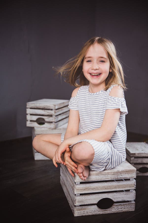 Portret van een gelukkig tienermeisje in de zomerkleding in studio Zij zit op de dozen, de wind die haar haar blazen royalty-vrije stock fotografie Portret van een gelukkig tienermeisje in de zomerkleding in studio Zij zit op de dozen, de wind die haar haar blazen royalty-vrije stock fotografie