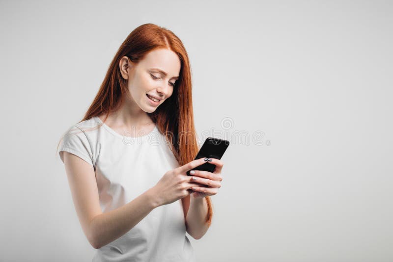 Portret van een het glimlachen de holdingssmartphone van de roodharigevrouw en het texting royalty-vrije stock fotografie Portret van een het glimlachen de holdingssmartphone van de roodharigevrouw en het texting royalty-vrije stock fotografie