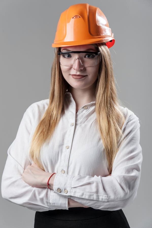 Portret van een jonge aantrekkelijke vrouw met blond haar in oranje helm op een neutrale grijze achtergrond royalty-vrije stock afbeelding Portret van een jonge aantrekkelijke vrouw met blond haar in oranje helm op een neutrale grijze achtergrond royalty-vrije stock afbeelding