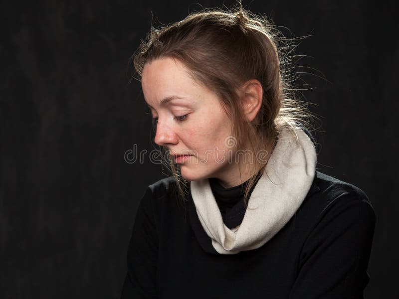Portrait of a young sad disoriented woman looking down, head is half-turned , grey background. Portrait of a young sad disoriented woman looking down, head is half-turned , grey background