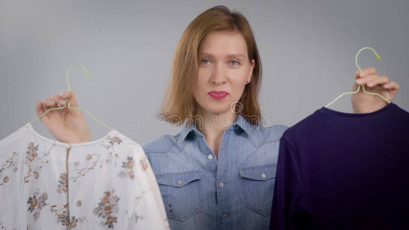 Portret van een jonge vrouw thuis Het meisje houdt de kleren in haar handen en bekijkt de camera met een glimlach