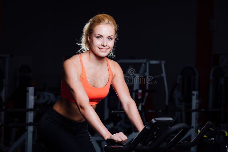 Portret van een leuke aardige vrouwelijke training op geschiktheid hometrainerdark bij gymnastiek royalty-vrije stock fotografie Portret van een leuke aardige vrouwelijke training op geschiktheid hometrainerdark bij gymnastiek royalty-vrije stock fotografie