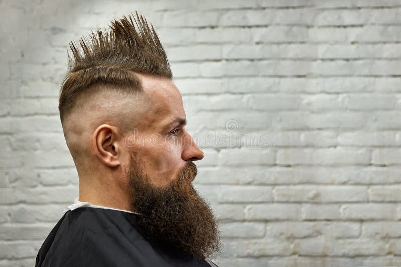 Portret van een mens met een mohawk en baard als kappersvoorzitter tegen een bakstenen muur sluit omhoog, baksteenachtergrond, ex royalty-vrije stock afbeeldingen Portret van een mens met een mohawk en baard als kappersvoorzitter tegen een bakstenen muur sluit omhoog, baksteenachtergrond, ex royalty-vrije stock afbeeldingen