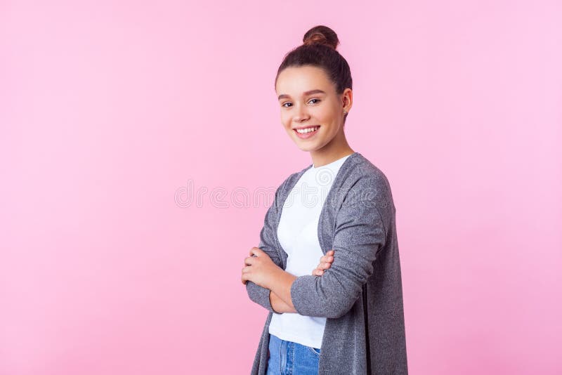 Portrait of nice brunette teenage girl with bun hairstyle in casual pullover and T-shirt standing with crossed arms and smiling at camera, happy in adolescence. studio shot isolated on pink background. Portrait of nice brunette teenage girl with bun hairstyle in casual pullover and T-shirt standing with crossed arms and smiling at camera, happy in adolescence. studio shot isolated on pink background