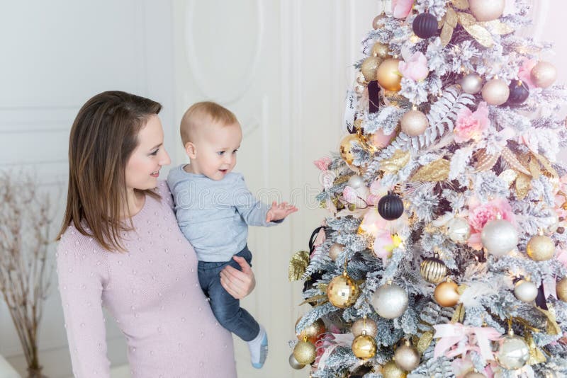 Portrait of beautiful young adult caucasian women wiht cute adorable little blond toddler boy enjoy trimming christmas tree in cozy living room at home . Happy mom with little son. New year holidays, family, mother, gift, sitting, kid, child, present, winter, xmas, snow, house, interior, indoor, love, festive, people, lifestyle, together, bauble, baby, two, decor, smile, couple, face, magic, spirit, card, background, decorated, surprise. Portrait of beautiful young adult caucasian women wiht cute adorable little blond toddler boy enjoy trimming christmas tree in cozy living room at home . Happy mom with little son. New year holidays, family, mother, gift, sitting, kid, child, present, winter, xmas, snow, house, interior, indoor, love, festive, people, lifestyle, together, bauble, baby, two, decor, smile, couple, face, magic, spirit, card, background, decorated, surprise