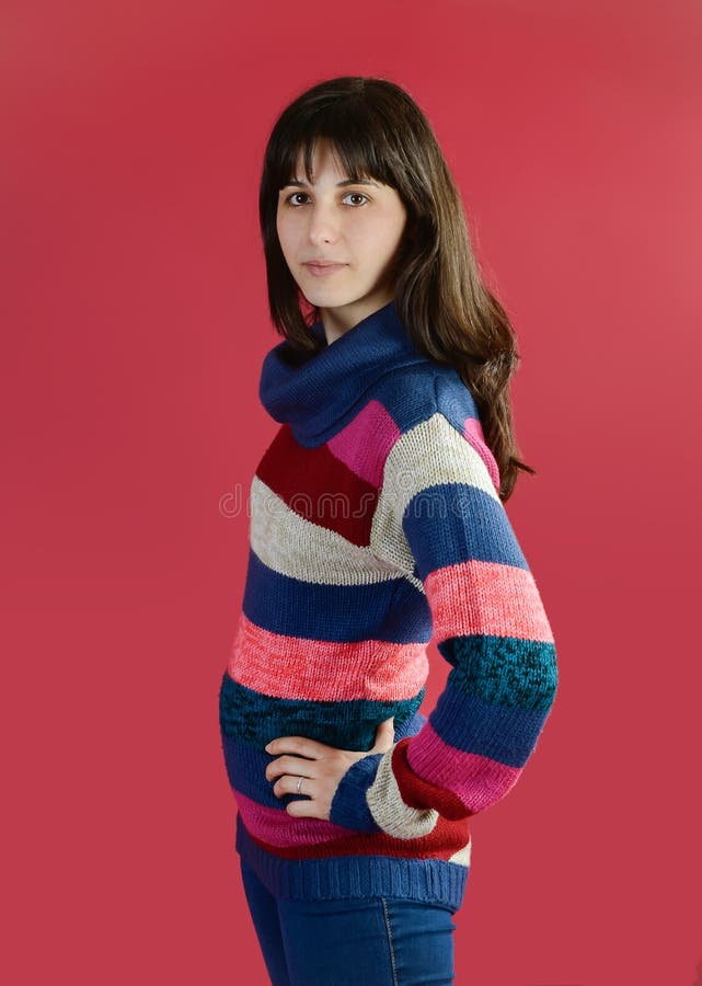 Portrait of a beautiful young woman in a striped sweater on a magenta background. Caucasian woman with long brunette hair posing in studio. Portrait of a beautiful young woman in a striped sweater on a magenta background. Caucasian woman with long brunette hair posing in studio.