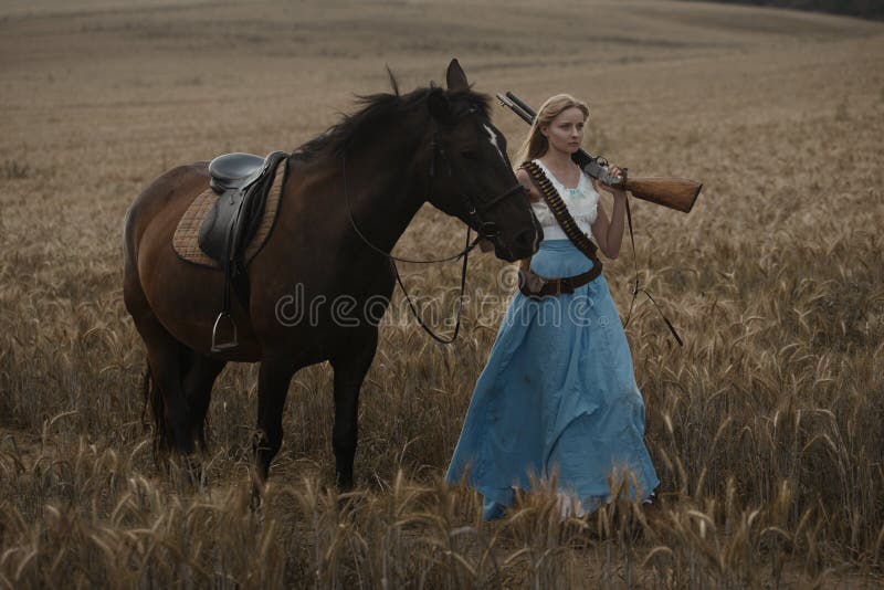 Portret van een mooie vrouwelijke veedrijfster met jachtgeweer die van het wilde westen een paard in het binnenland berijden royalty-vrije stock foto Portret van een mooie vrouwelijke veedrijfster met jachtgeweer die van het wilde westen een paard in het binnenland berijden royalty-vrije stock foto