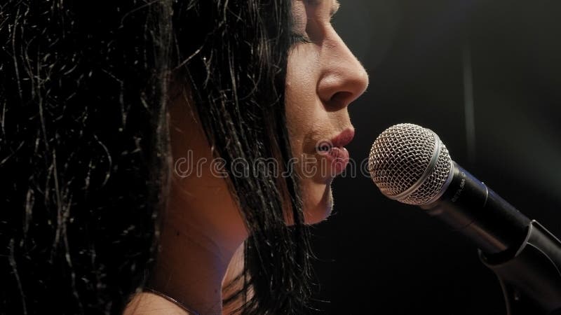 Portret van een mooie zanger met lang haar op een donker podium in de schijnwerpers.