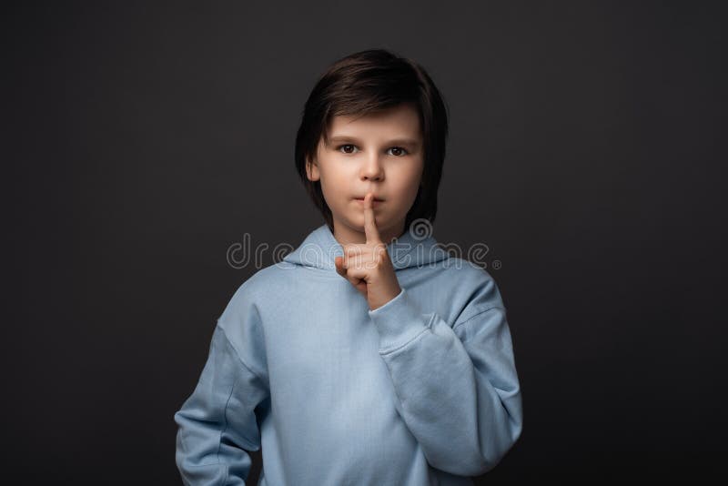 Portrait of Cute boy 10-12 years old, dressed in casual clothes holding index finger on lips. Silence and secret concept. Studio shot, gray background. Human emotions, facial expression concept. Portrait of Cute boy 10-12 years old, dressed in casual clothes holding index finger on lips. Silence and secret concept. Studio shot, gray background. Human emotions, facial expression concept