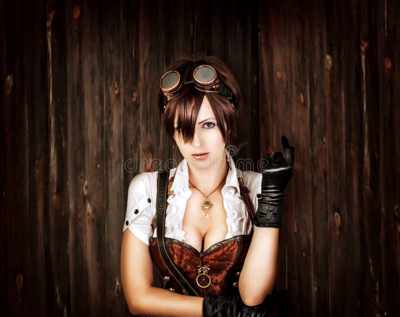 Portrait of a steampunk woman with big breast wearing vintage corset and retro goggles on old wooden background. Portrait of a steampunk woman with big breast wearing vintage corset and retro goggles on old wooden background