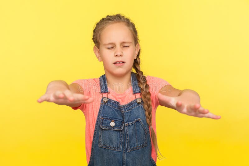 Portrait of confused disoriented little girl with braid in denim overalls walking blind with closed eyes and outstretched hands, searching way. indoor studio shot isolated on yellow background. Portrait of confused disoriented little girl with braid in denim overalls walking blind with closed eyes and outstretched hands, searching way. indoor studio shot isolated on yellow background