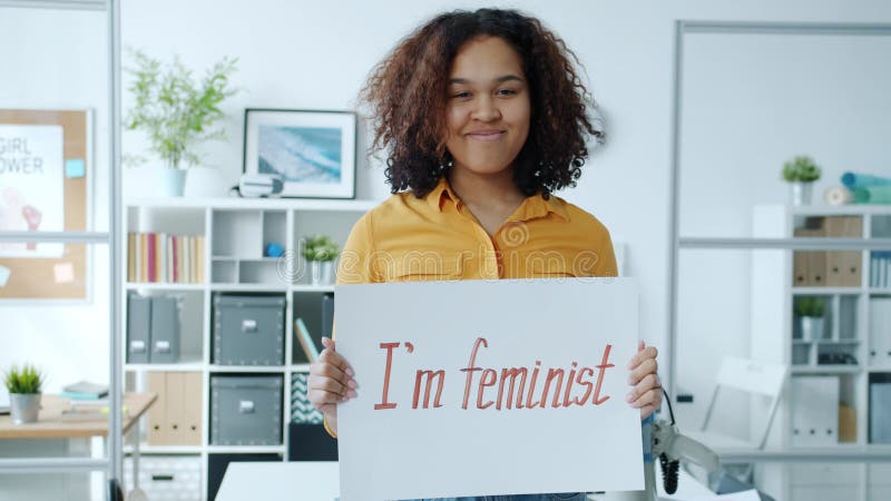 Portret van een vrolijk afrikaans - amerikaans meisje met een feministische banner die lacht binnen in zijn eentje