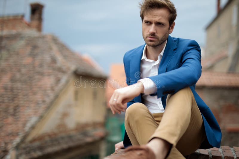 Portrait of a seated fashion man looking away against urban background. Portrait of a seated fashion man looking away against urban background