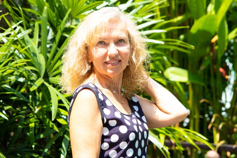Portret van een 50 éénjarigenvrouw in de zomer tegen een achtergrond van groene tropische palmen stock afbeeldingen Portret van een 50 éénjarigenvrouw in de zomer tegen een achtergrond van groene tropische palmen stock afbeeldingen