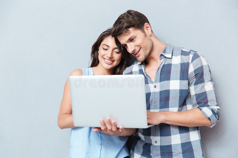 Portret van gelukkig jong paar die laptop over grijze achtergrond met behulp van stock foto Portret van gelukkig jong paar die laptop over grijze achtergrond met behulp van stock foto