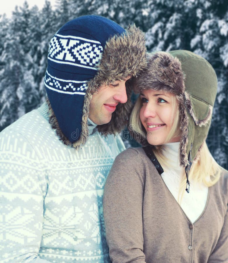 Portret van gelukkig vrij jong glimlachend paar die in warme de winterdag hoed en gebreide sweater over sneeuwbomenbos dragen royalty-vrije stock foto Portret van gelukkig vrij jong glimlachend paar die in warme de winterdag hoed en gebreide sweater over sneeuwbomenbos dragen royalty-vrije stock foto