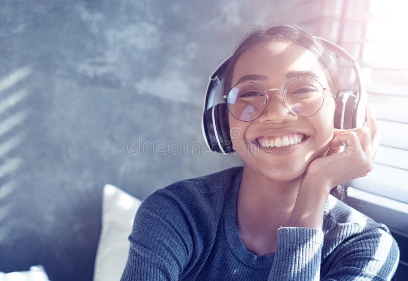 Portret van glimlachend meisje met hoofdtelefoons die aan muziek luisteren terwijl thuis het zitten op bank stock fotografie Portret van glimlachend meisje met hoofdtelefoons die aan muziek luisteren terwijl thuis het zitten op bank stock fotografie
