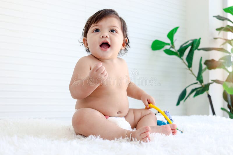 Portrait of smiling crawling baby sits on fluffy white rug, little cute kid girl playing with developmental toys, happy daughter child playing and laughing, love in family, childhood care and learning. Portrait of smiling crawling baby sits on fluffy white rug, little cute kid girl playing with developmental toys, happy daughter child playing and laughing, love in family, childhood care and learning