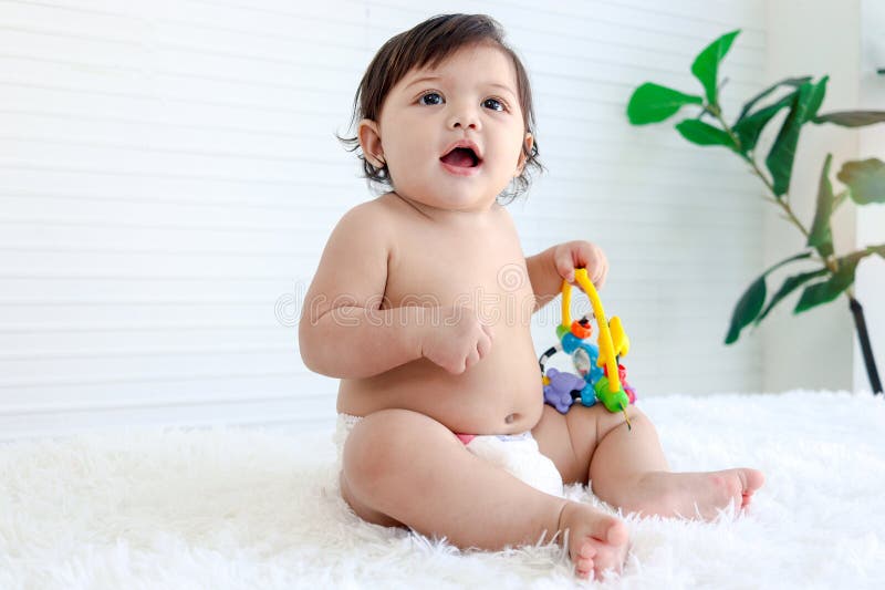 Portrait of smiling crawling baby sits on fluffy white rug, little cute kid girl playing with developmental toys, happy daughter child playing and laughing, love in family, childhood care and learning. Portrait of smiling crawling baby sits on fluffy white rug, little cute kid girl playing with developmental toys, happy daughter child playing and laughing, love in family, childhood care and learning