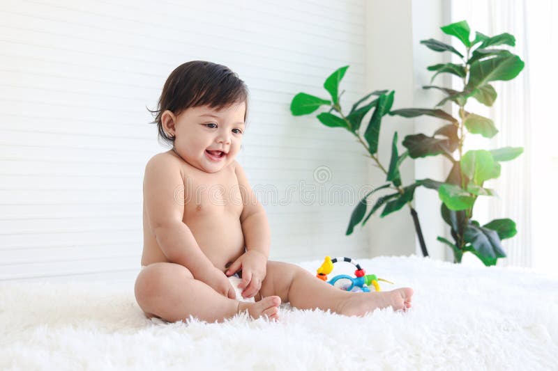 Portrait of smiling crawling baby sits on fluffy white rug, little cute kid girl playing with developmental toys, happy daughter child playing and laughing, love in family, childhood care and learning. Portrait of smiling crawling baby sits on fluffy white rug, little cute kid girl playing with developmental toys, happy daughter child playing and laughing, love in family, childhood care and learning