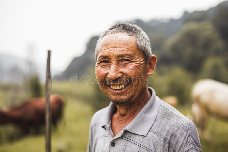 Portret van glimlachende landbouwer met vee op de achtergrond, landelijk China, Shanxi-Provincie