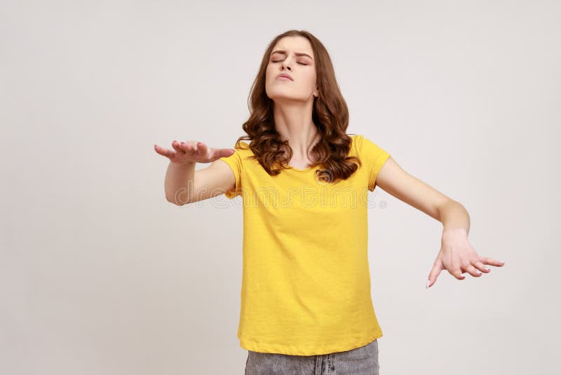 Portrait of blind disoriented brown haired teenager girl in yellow casual T-shirt walking with closed eyes, reaching out hands to find lost way. Indoor studio shot isolated on gray background. Portrait of blind disoriented brown haired teenager girl in yellow casual T-shirt walking with closed eyes, reaching out hands to find lost way. Indoor studio shot isolated on gray background.