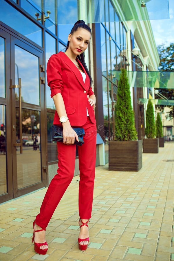 Portret van jonge schitterende dame met hoge poneystaart in rood kostuum en high-heeled schoenen die zich voor weerspiegeld winke stock fotografie Portret van jonge schitterende dame met hoge poneystaart in rood kostuum en high-heeled schoenen die zich voor weerspiegeld winke stock fotografie