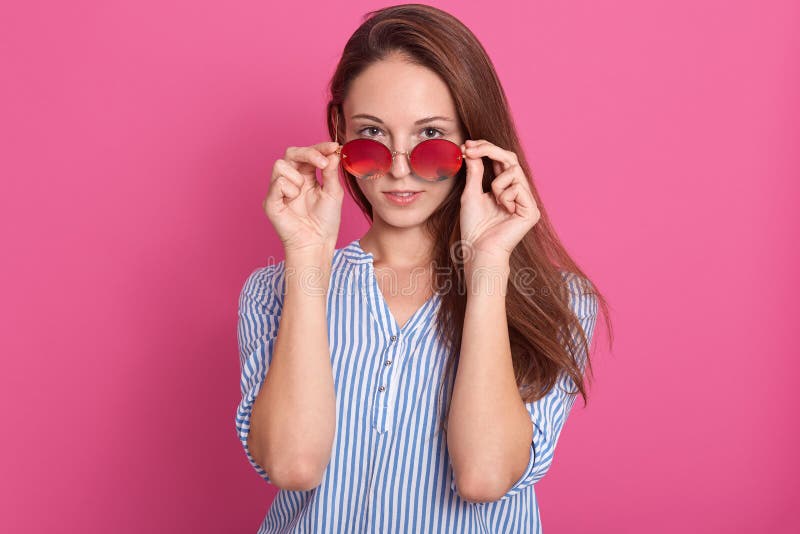 Portret van manier het aantrekkelijke vrouw gluren over zonnebril Het vrouwelijke model stellen tegen roze studioachtergrond, mod royalty-vrije stock fotografie Portret van manier het aantrekkelijke vrouw gluren over zonnebril Het vrouwelijke model stellen tegen roze studioachtergrond, mod royalty-vrije stock fotografie
