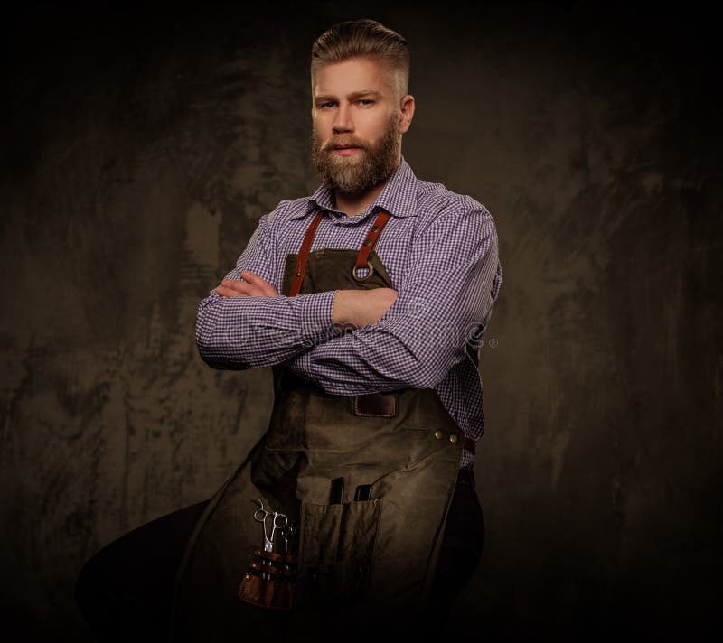 Portret van modieuze kapper met baard en professionele die hulpmiddelen op een donkere achtergrond wordt geïsoleerd stock fotografie Portret van modieuze kapper met baard en professionele die hulpmiddelen op een donkere achtergrond wordt geïsoleerd stock fotografie