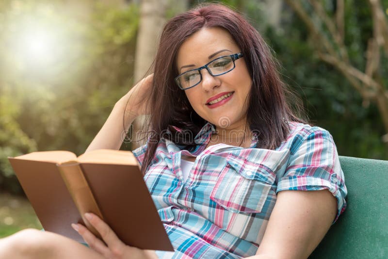 Portret van mooie jonge vrouw die een boek op een bank in park, lichteffect lezen stock fotografie Portret van mooie jonge vrouw die een boek op een bank in park, lichteffect lezen stock fotografie