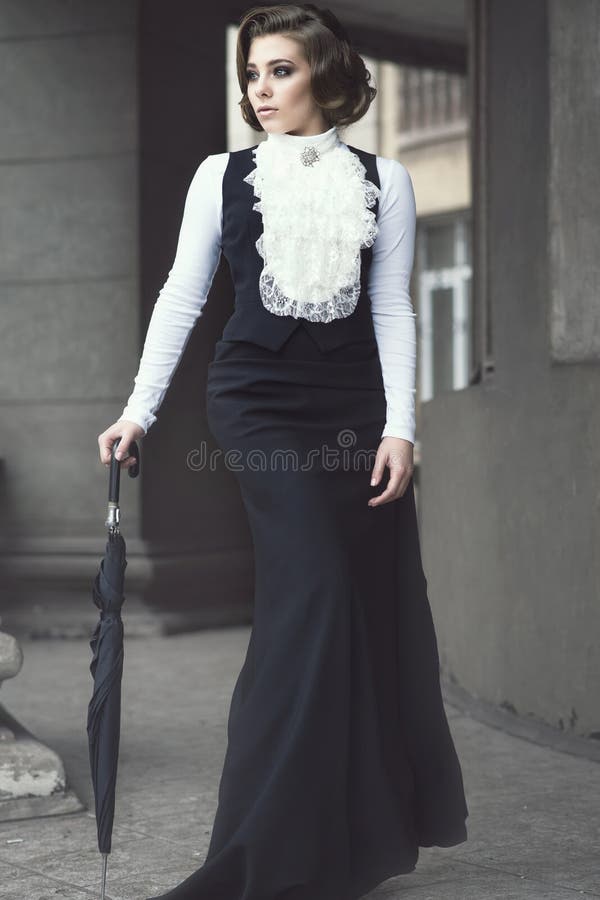Portret van schitterende vrouw met elegant Victoriaans kapsel die ouderwetse toga dragen die onder de pijlers lopen stock foto Portret van schitterende vrouw met elegant Victoriaans kapsel die ouderwetse toga dragen die onder de pijlers lopen stock foto