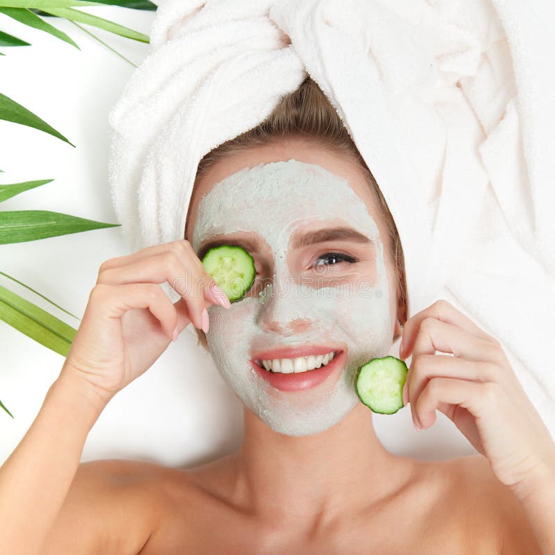 Portrait of beauty woman laying with towel on the head, cucumber on her eyes, facial mask. Spa therapy. Relax. White background. Portrait of beauty woman laying with towel on the head, cucumber on her eyes, facial mask. Spa therapy. Relax. White background