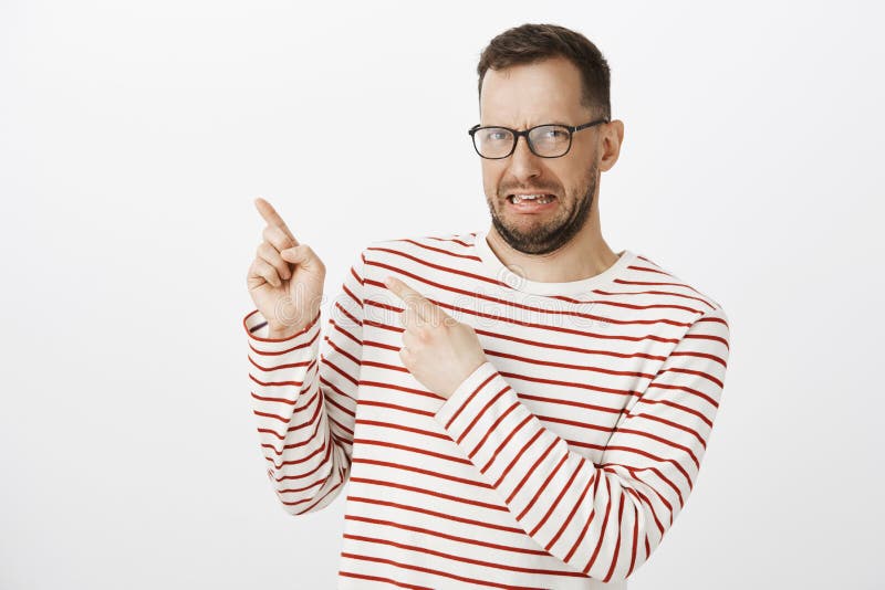 Portret zdegustowany nierad śmieszny caucasian facet w czarnych modnych szkłach, wskazuje przy górnym lewym kątem i zdjęcia stock Portret zdegustowany nierad śmieszny caucasian facet w czarnych modnych szkłach, wskazuje przy górnym lewym kątem i zdjęcia stock