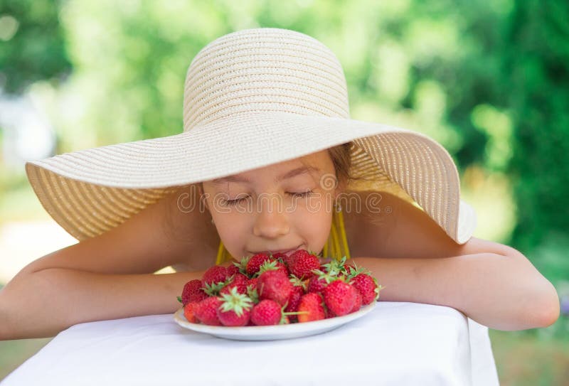 Portret Śliczna preteen dziewczyna w dużym kapeluszu je truskawki przy letnim dniem fotografia stock Portret Śliczna preteen dziewczyna w dużym kapeluszu je truskawki przy letnim dniem fotografia stock