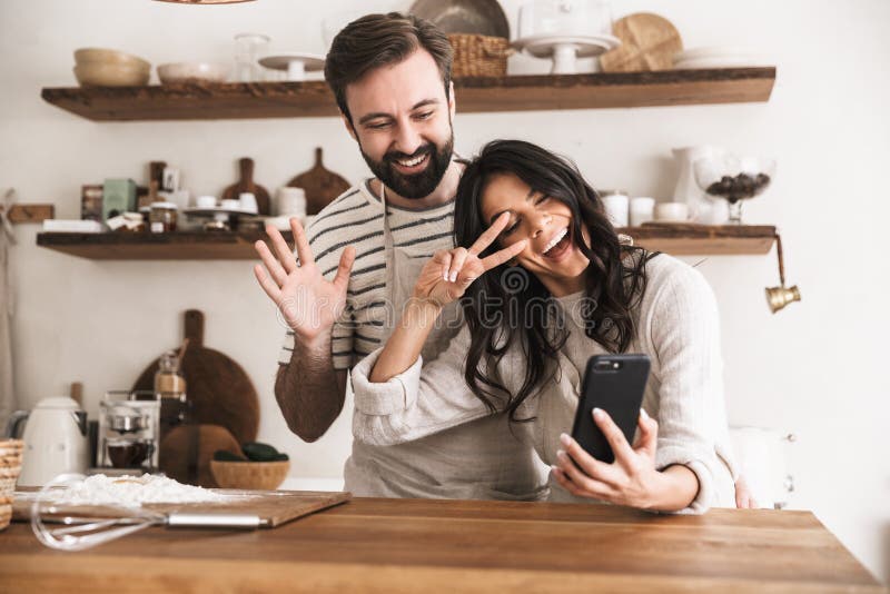 Portret ściska wpólnie i trzyma smartphone uśmiechnięta para podczas gdy gotujący w kuchni w domu zdjęcie royalty free Portret ściska wpólnie i trzyma smartphone uśmiechnięta para podczas gdy gotujący w kuchni w domu zdjęcie royalty free