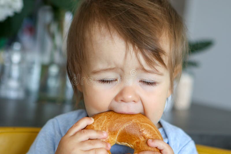 Portret śmieszna mała chłopiec je dużego bagel z zamkniętymi oczami, zabawy twarzy wyrażenie zdjęcie royalty free Portret śmieszna mała chłopiec je dużego bagel z zamkniętymi oczami, zabawy twarzy wyrażenie zdjęcie royalty free