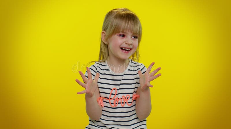 Portrait of funny playful blonde kid child shouting, raising hands in gesture I did it, celebrating success, winning and goal achievemen on yellow studio background. Teenager children girl emotions. Portrait of funny playful blonde kid child shouting, raising hands in gesture I did it, celebrating success, winning and goal achievemen on yellow studio background. Teenager children girl emotions