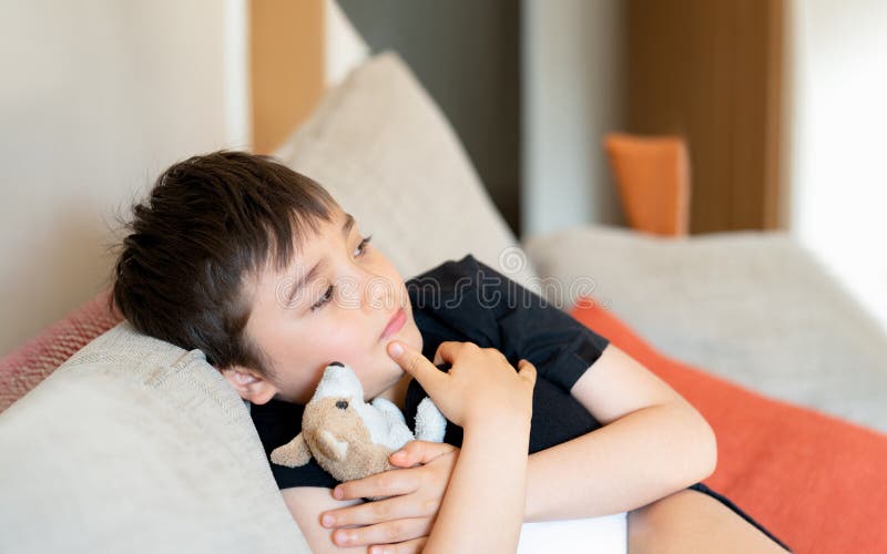 Portrait Kid sitting on sofa with dog toy watching TV,Young boy sitting on couch looking out deep in thought. Positive Child relaxing at home on weekend,Children lifestyle concept. Portrait Kid sitting on sofa with dog toy watching TV,Young boy sitting on couch looking out deep in thought. Positive Child relaxing at home on weekend,Children lifestyle concept