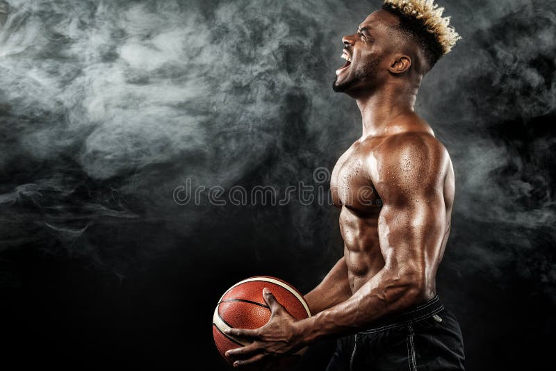 Portretul baschetbalistului sportiv afroamerican cu o minge peste fundalul negru. tânăr potrivit în sport royalty free stock photography
