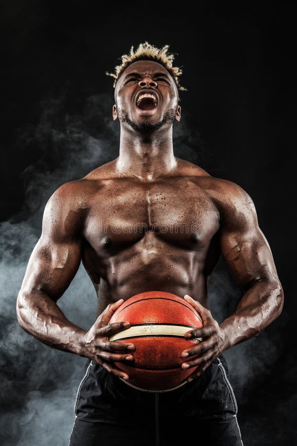 Portretul baschetbalistului sportiv afroamerican cu o minge peste fundalul negru. tânăr potrivit în sport royalty free stock photos