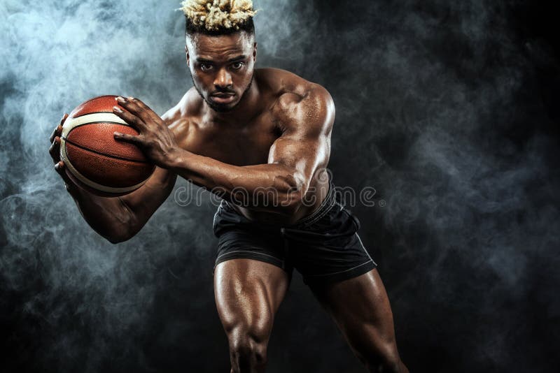 Portretul baschetbalistului sportiv afroamerican cu o minge peste fundalul negru. tânăr potrivit în sport stock photography