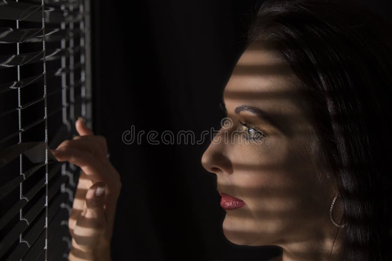Portretul unei femei care stă în întuneric uitându-se prin jaluzele stock images
