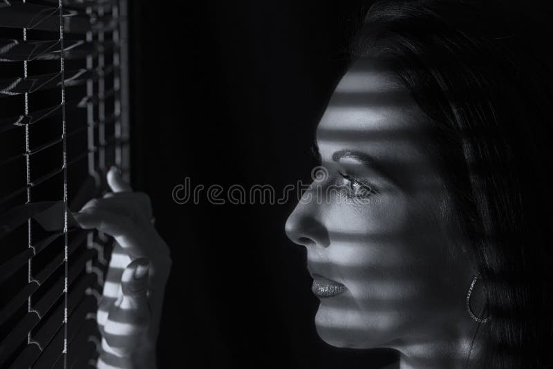 Portretul unei femei care stă în întuneric uitându-se prin jaluzele stock photos