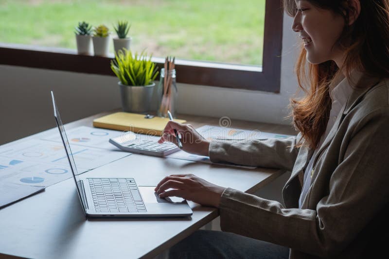 Portretul unui contabil feminin care utilizează un calculator și un laptop pentru a calcula echilibrul utilizând grafice pentru cl royalty free stock image