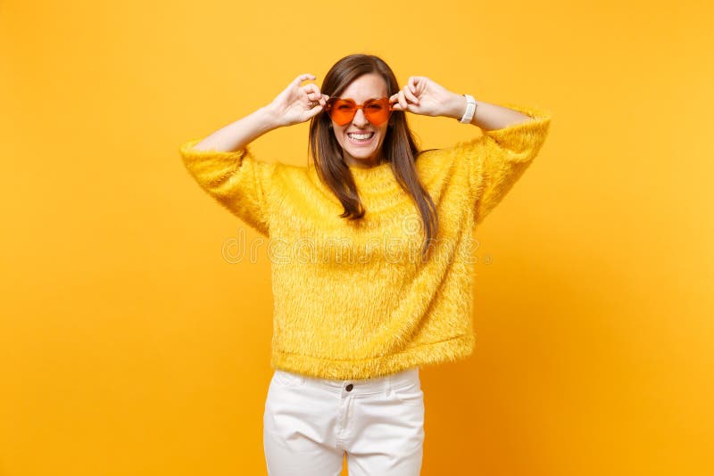 Porträt des Lachens der glücklichen jungen Frau in der Pelzstrickjacke, weiße Hosen, die orange Brillen des Herzens lokalisiert a lizenzfreie stockbilder Porträt des Lachens der glücklichen jungen Frau in der Pelzstrickjacke, weiße Hosen, die orange Brillen des Herzens lokalisiert a lizenzfreie stockbilder