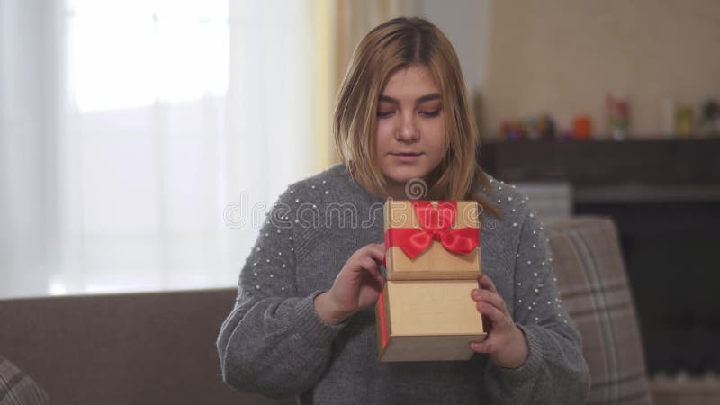 Porträt glückliches frohes bbw öffnenden Geschenks, das auf Sofa im Raum sitzt