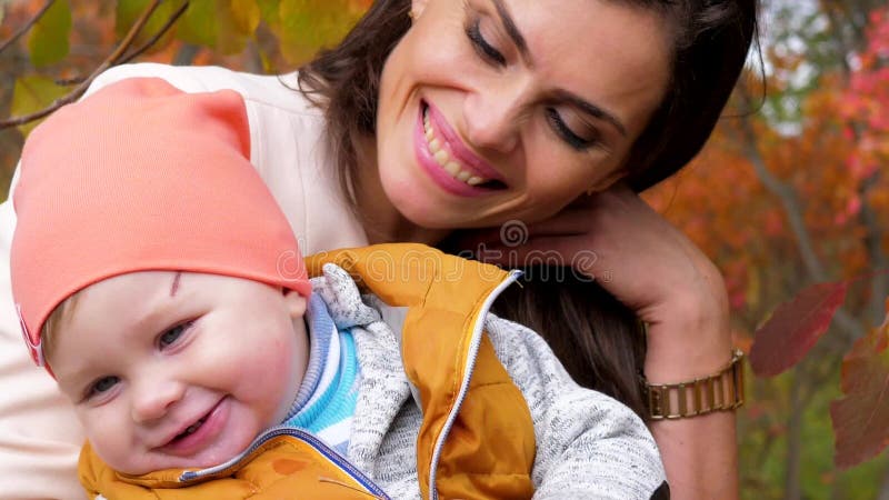 Porträt der glücklichen Familie, Mutter nahe Baby mit geifernder Nahaufnahme auf Hintergrund von gelben Bäumen im Herbststadtpark